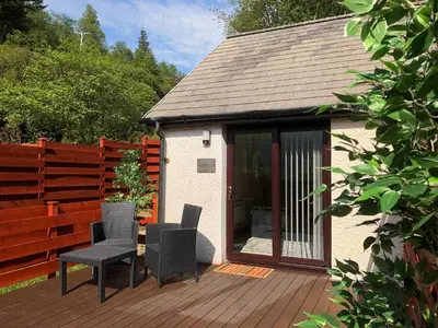 a patio with two chairs and a table on a deck at The Wee Ludging - A Cosy Riverside Cottage for Two in Dunoon