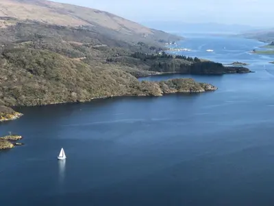 a sail boat in the middle of a large lake at The Wee Ludging - A Cosy Riverside Cottage for Two in Dunoon