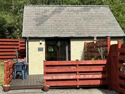 a small house with a wooden fence and a bench at The Wee Ludging - A Cosy Riverside Cottage for Two in Dunoon