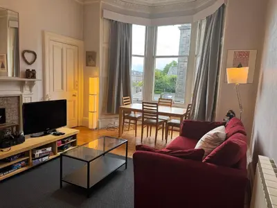a living room with a red couch and a table at Classic Edinburgh Flat in the heart of Morningside in Edinburgh