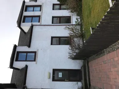 a white building with black windows and a brick wall at Greannan Upper Self Catering Apartment in Blackwaterfoot