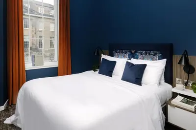 a bedroom with a white bed with blue walls and a window at Heeton Concept Aparthotel Edinburgh Queen Street in Edinburgh
