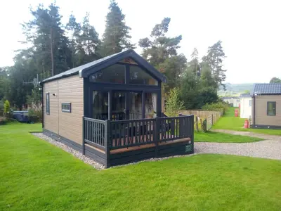 a small building with a deck on the grass at Callander Woods Holiday Park in Callander