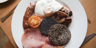 a plate of breakfast food with eggs bacon and meat at Creebridge House Hotel in Newton Stewart