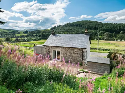 a stone cottage with a field of flowers at Nettlebush Cottage-Uk5629 in Drummelzier