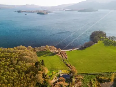 an aerial view of a green field next to the water at Strathcashel Cottage in Rowardennan