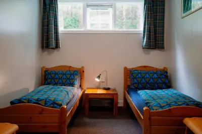two beds in a room with a table and a window at Glencoe Youth Hostel in Ballachulish