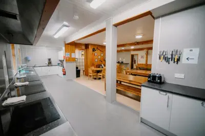 a kitchen with white cabinets and a dining room at Glencoe Youth Hostel in Ballachulish