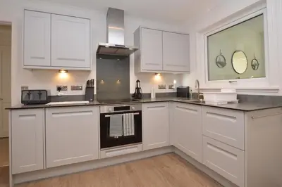 a kitchen with white cabinets and a stove top oven at Dunbheag Cottage in Strone