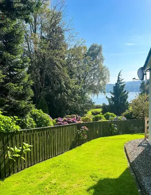 a fence in a yard with green grass and flowers at Dunbheag Cottage in Strone