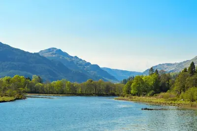a river with trees and mountains in the background at Dunbheag Cottage in Strone
