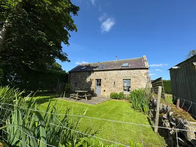 an old stone cottage with a picnic table in the yard at Charming cottage with loch and hill views nr Edinburgh in Cobbinshaw