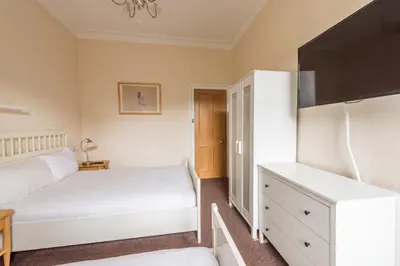 a bedroom with two white beds and a dresser at 3 bed overlooking meadows park in Edinburgh