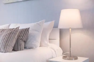 a bed with white pillows and a table with a lamp at Peebles House - Coorie Doon Apartments in Ayr