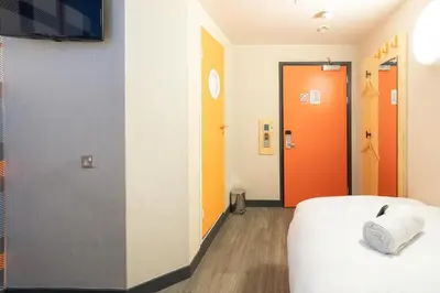 a room with a bed and a hallway with orange doors at easyHotel Glasgow City in Glasgow