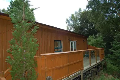 a wooden cabin with a porch and a tree at Waterfall Lodge - private waterfall and sauna in Killin