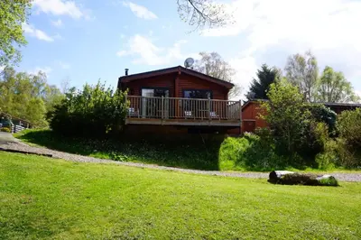 a log cabin with a deck on a grass field at Luxury woodland Alder Lodge in Killin
