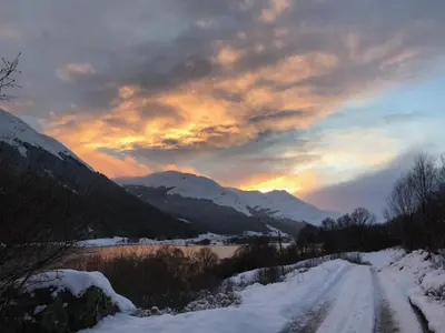 a snow covered road with a sunset in the mountains at Hillside Log cabin, Ardoch Lodge, Strathyre in Strathyre