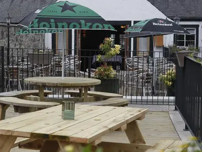 two wooden picnic tables with chairs and an umbrella at Elphinstone Hotel in Biggar