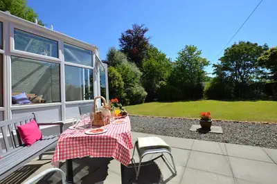 a picnic table on the porch of a house at Cedar Cottage in Dunoon