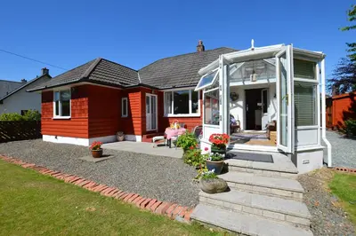 a small house with a greenhouse in front of it at Cedar Cottage in Dunoon