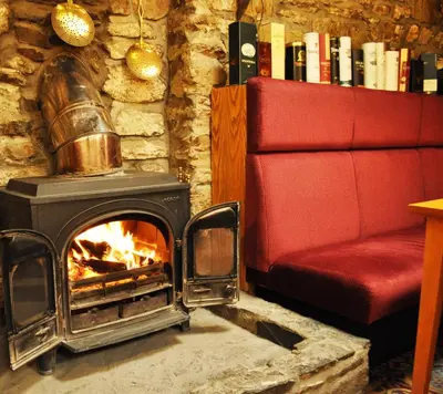 a fireplace in a living room with a red couch at The Galley Of Lorne Inn in Ardfern