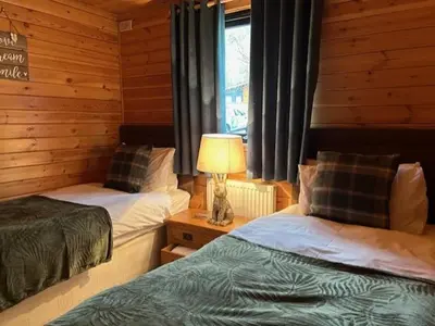a bedroom with two beds and a lamp and a window at Balquhidder Braes Holiday Park Lodges, mostly with Hot Tubs and pet friendly, EV facilities in Lochearnhead