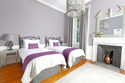 two beds in a white room with a fireplace at Drylaw House, Grade A Listed Mansion near City Centre in Edinburgh