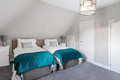 a white bedroom with two beds and a chandelier at Drylaw House, Grade A Listed Mansion near City Centre in Edinburgh