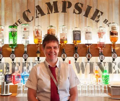 a man standing in front of a bar with glasses of beer at The Coachman Hotel in Kilsyth