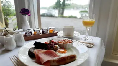 a table with a plate of breakfast food and a glass of wine at Dungallan Country House in Oban