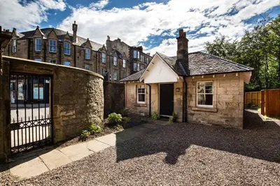 an old stone house with a gate and a building at Trinity Lodge - Home with Private Garden and Parking in Edinburgh