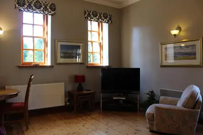 a living room with a flat screen tv and two windows at Stables Lodge in Balloch