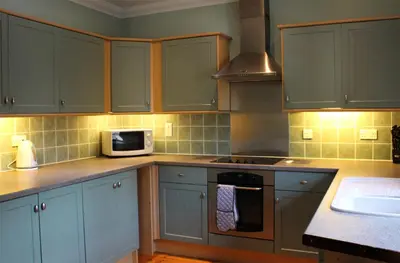 a kitchen with blue cabinets and a microwave at Smiddy Lodge in Balloch