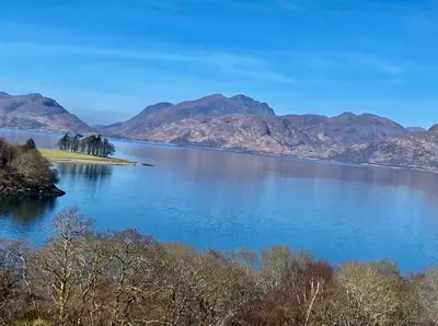 an island in the middle of a lake with mountains at Hunters Lodge Apartments in Ballachulish