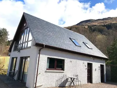 a white house with a black roof and a table at Hunters Lodge Apartments in Ballachulish