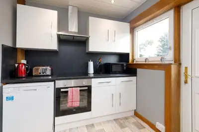a kitchen with white cabinets and a window at Lomond Serviced Apartments- Inglewood in Alloa