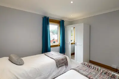 a bedroom with a bed with blue curtains and a window at Lomond Serviced Apartments- Inglewood in Alloa