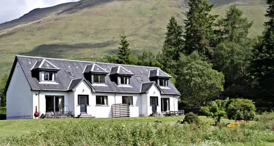 a white house with a mountain in the background at Stob Binnein Cottage in Crianlarich