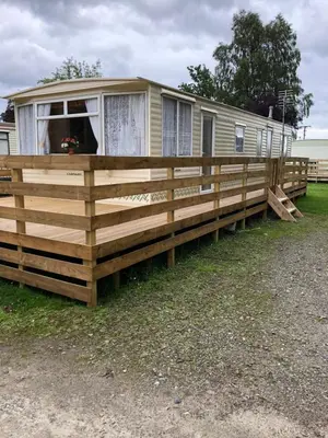 a mobile home with a large wooden deck at 57 Glenfinart Caravan Park in Ardentinny