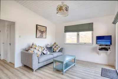 a living room with a couch and a tv at Gamekeeper Lodge loch and mountain view free wifi in Crianlarich