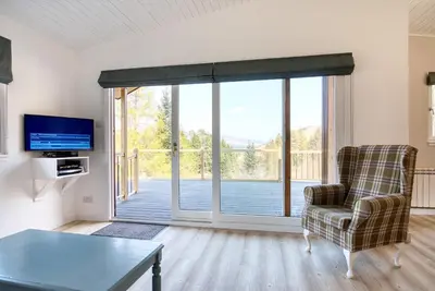 a living room with a chair and a sliding glass door at Gamekeeper Lodge loch and mountain view free wifi in Crianlarich