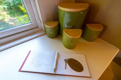 a book on a window sill with three green cups at Kestrel Lodge with mountain view free wifi in Crianlarich