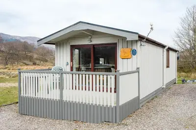 a small white shed with a porch and a fence at Lapwing Lodge with loch and mountain view in Crianlarich