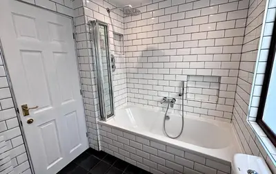 a white tiled bathroom with a tub and a shower at Lapwing Lodge with loch and mountain view in Crianlarich