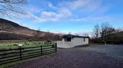 a building with a fence next to a field with sheep at Lapwing Lodge with loch and mountain view in Crianlarich