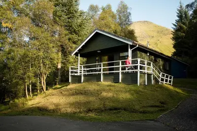 a woman standing on the porch of a house at Osprey Lodge with river and mountain view in Crianlarich