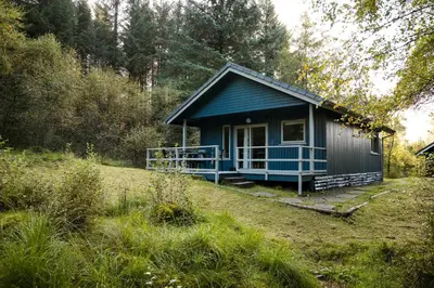 a blue cottage in the middle of a field at Otter with mountain view and enclosed decking in Crianlarich