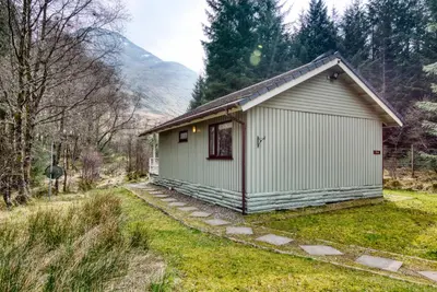 a small white building in the middle of a field at Otter with mountain view and enclosed decking in Crianlarich