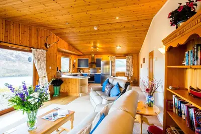 a living room with a couch and a kitchen at Raven Lodge with beautiful views of Loch Dochart in Crianlarich